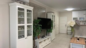 A modern living room with a flat-screen TV, white cabinets, and a small table with a potted plant. - TópART Apartman I :Apartment - first floor (Balatonfenyves)
