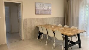 A dining area with a wooden table and white chairs, a painting on the wall, and a door leading to another room. - TópART Apartman I :Apartment - first floor (Balatonfenyves)