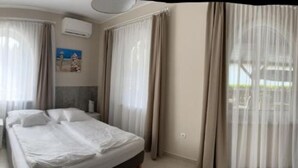 A hotel room with a bed, curtains, an air conditioning unit, and a painting on the wall. - TópART Apartman I :Apartment - first floor (Balatonfenyves)