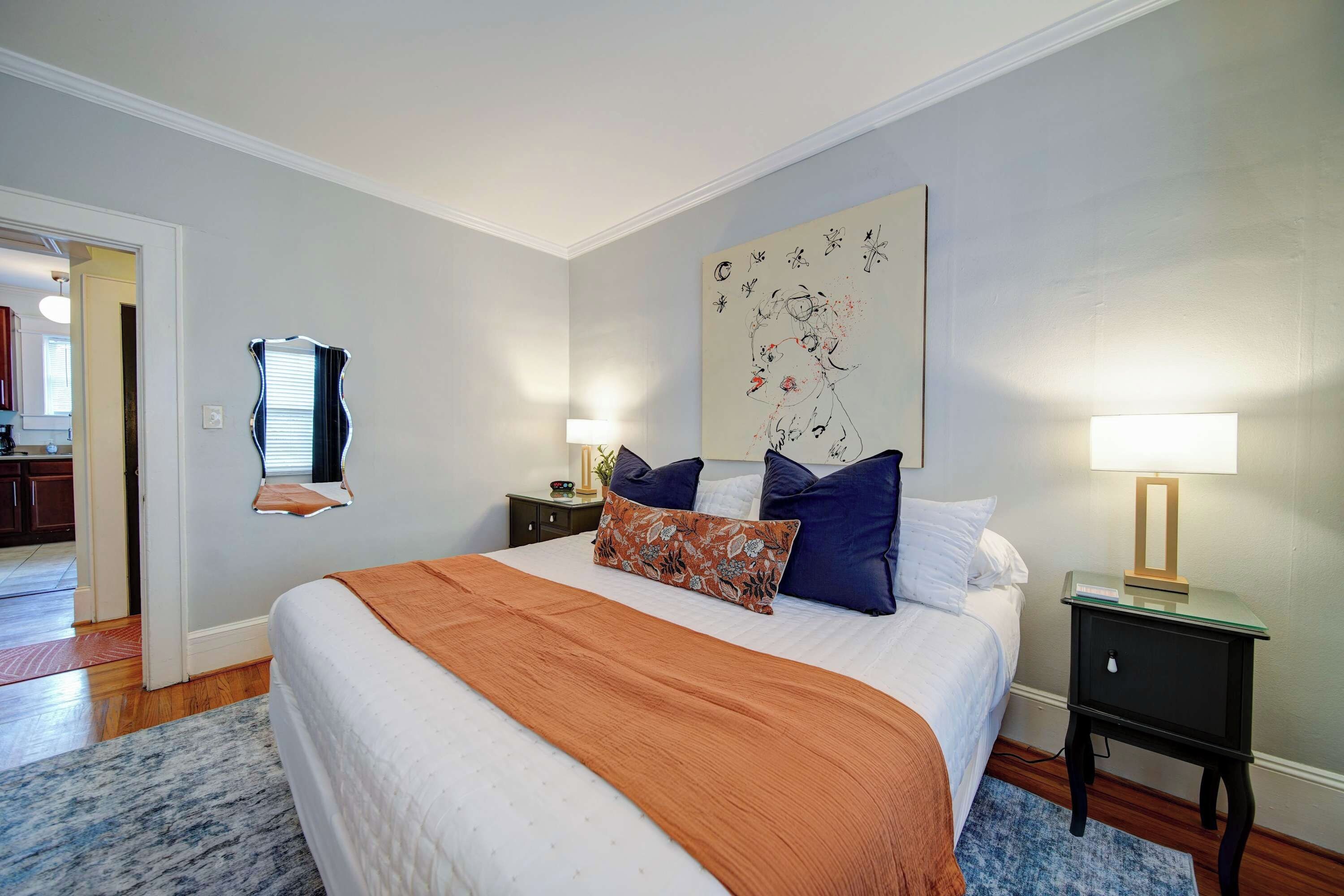 A hotel room with a bed, two bedside tables, a nightstand, a large abstract painting, and a door leading to another room.
