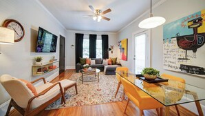 Una sala moderna con sofá, sillas, una mesita de centro y una zona de comedor con mesa y sillas de vidrio.