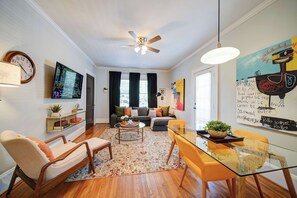 A modern living room with a sofa, chairs, a coffee table, and a dining area with a glass table and chairs. - The Home Collection: Pet Friendly Dilworth 2BR w/ Balcony near Atrium CMC (Charlotte)