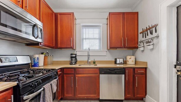 Una cocina con armarios de madera, lavavajillas de acero inoxidable, estufa y microondas.