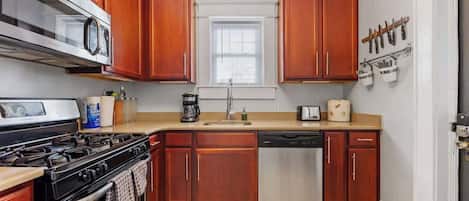 Una cocina con armarios de madera, lavavajillas de acero inoxidable, estufa y microondas.