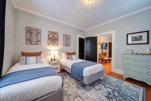 Une chambre d’hôtel avec deux lits, un bureau, une chaise et une commode. Il y a trois tableaux accrochés au mur.