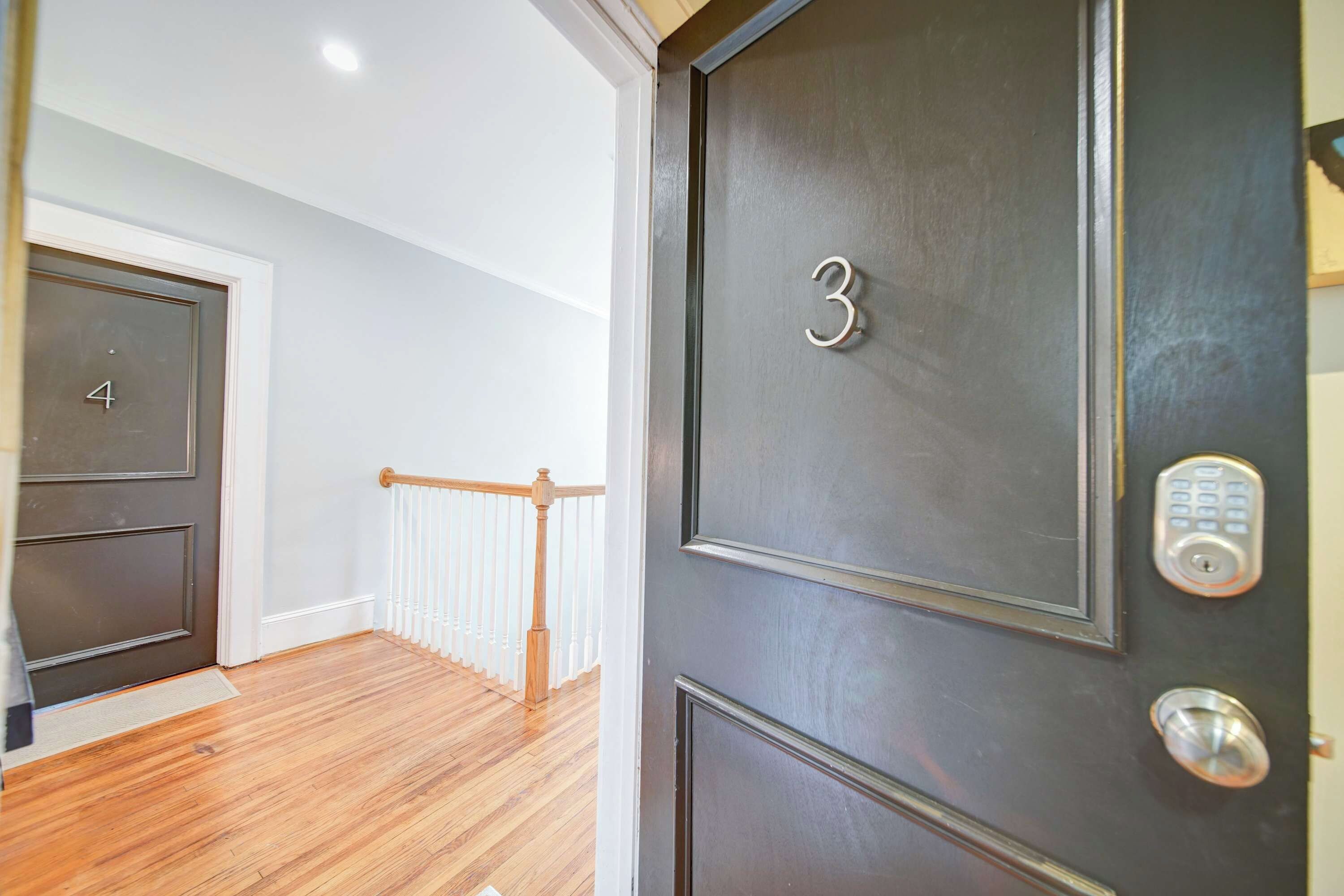 A dark-colored door with the number 3, a keypad lock, and a wooden railing in a hallway.