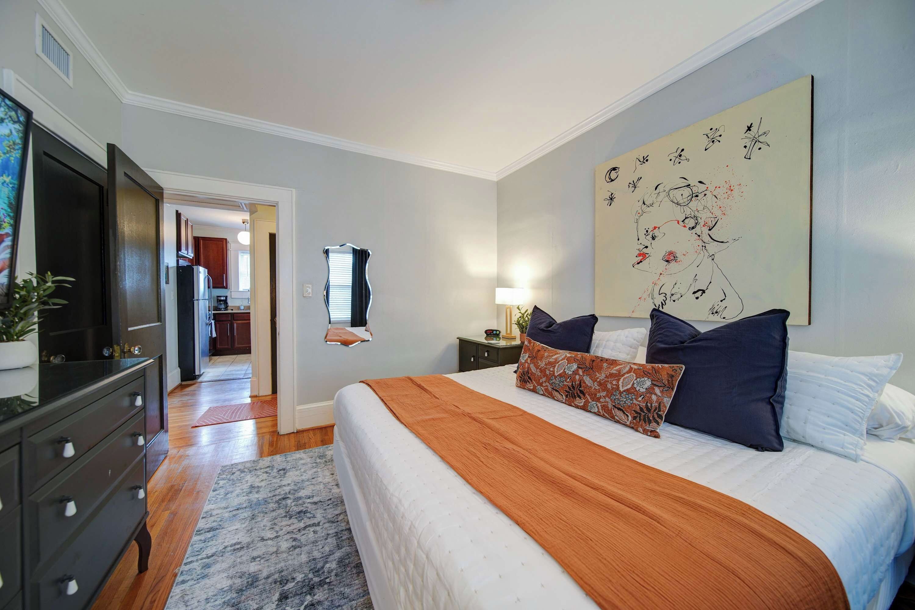 Un dormitorio con una cama grande, un aparador, una mesita de noche y una obra de arte colgada en la pared.