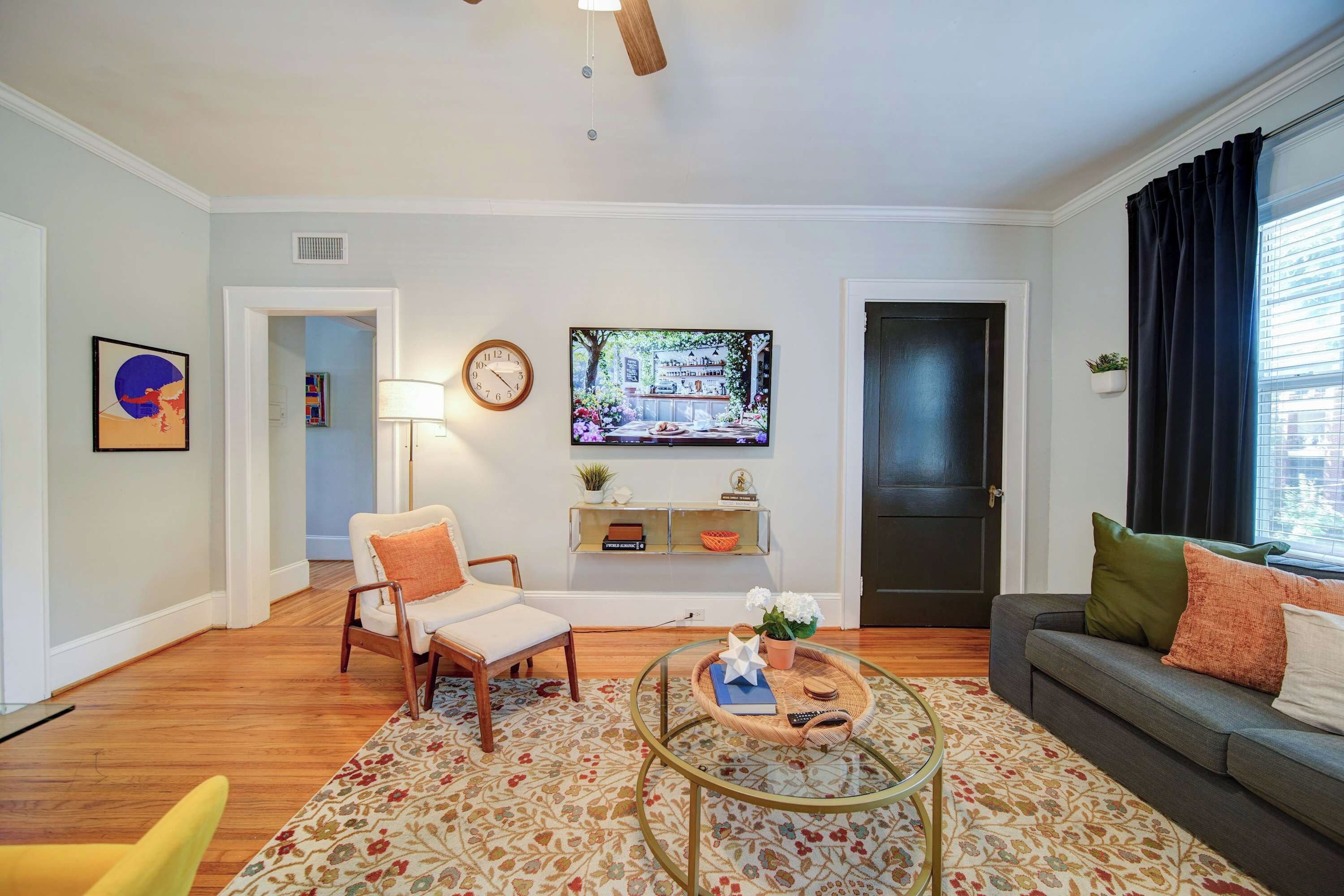 Uma sala de estar com sofá, poltrona, mesa de centro, televisão e uma porta.
