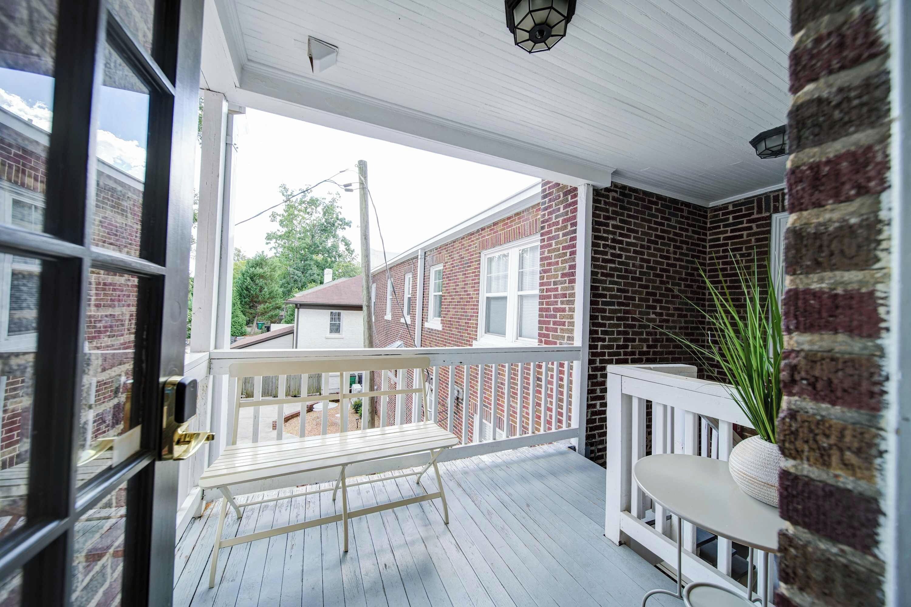 A covered porch with a white railing, a bench, and a potted plant.