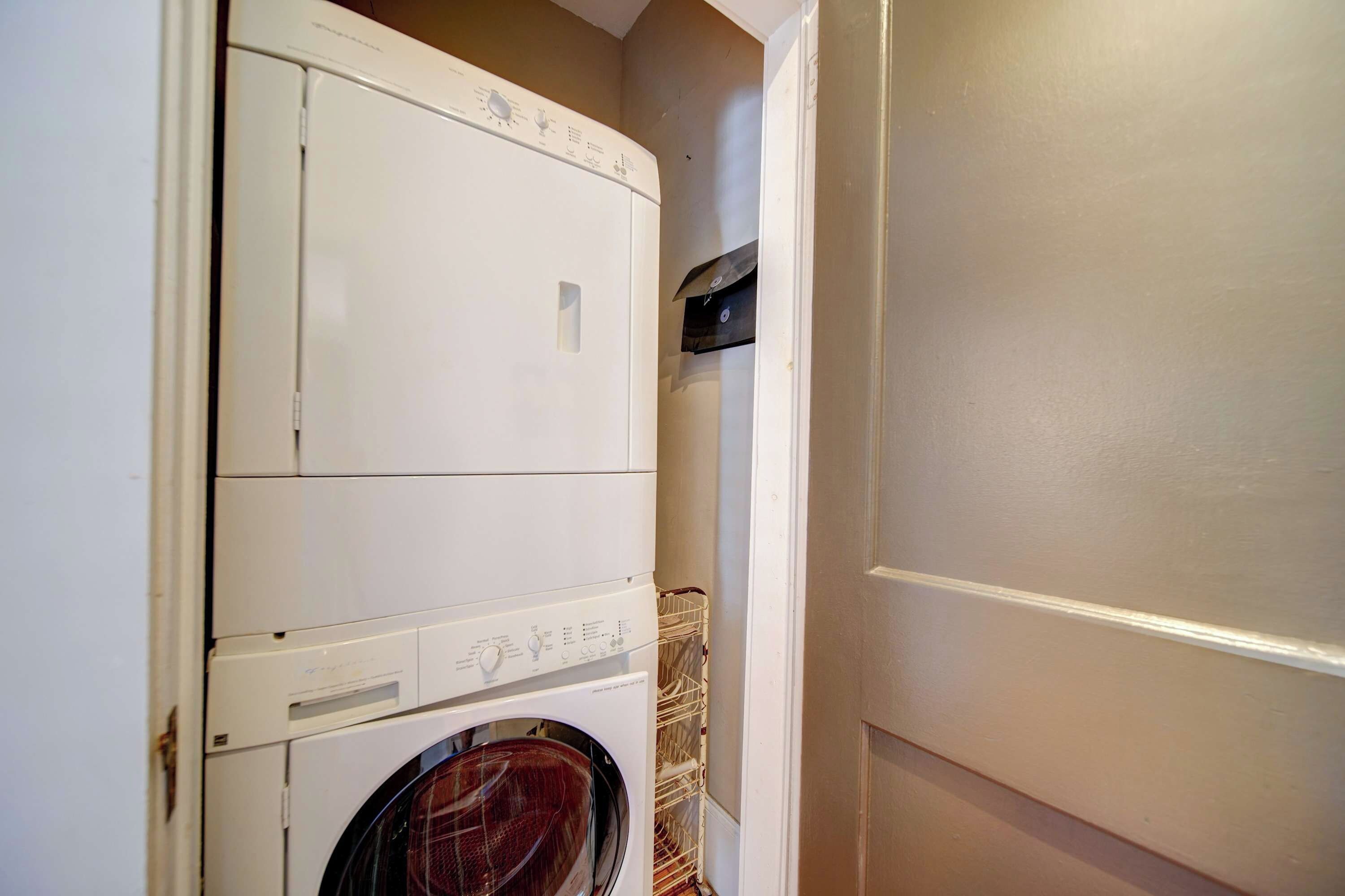 A compact, white laundry room with a washing machine and dryer, a small shelf, and a door.