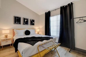A bedroom with a bed, bedside table, lamp, and a window with curtains.
