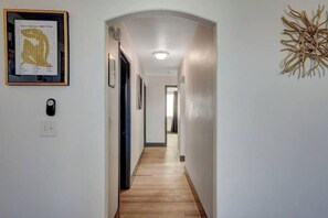 A hallway with a wooden floor, a framed artwork on the left, and a wall decoration on the right. - Amazing 4BD Home w/Pool, Arcades, & Billiard! (Las Vegas)
