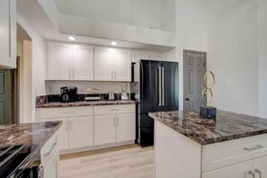 A modern kitchen with white cabinets, a black refrigerator, and a marble countertop.