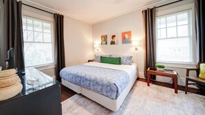 Ein Schlafzimmer mit Bett, Nachttischen, einem Fenster mit Vorhängen und Wandbildern.