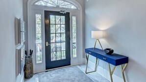 A hallway with a dark blue door, a white wall, a blue console table with a lamp, and a patterned rug.