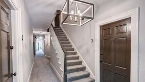 A hallway with a staircase, a door, and a light fixture.