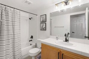 A modern bathroom with a white sink, vanity, and a large mirror. There is a shower curtain, a toilet, and a bathtub.