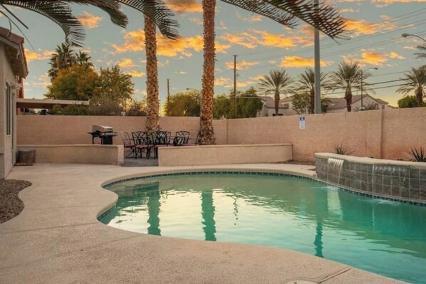A swimming pool with a curved edge, surrounded by a concrete deck and palm trees.