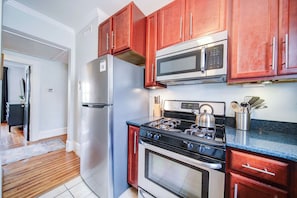 Una cocina con refrigerador de acero inoxidable, microondas, estufa a gas y alacenas de madera.
