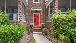 A two-story brick building with a red door, a small porch, and a pathway leading to the entrance. - The Home Collection: Historic Step-Free 2BR, Pet Friendly & Close to  Atrium CMC (Charlotte)