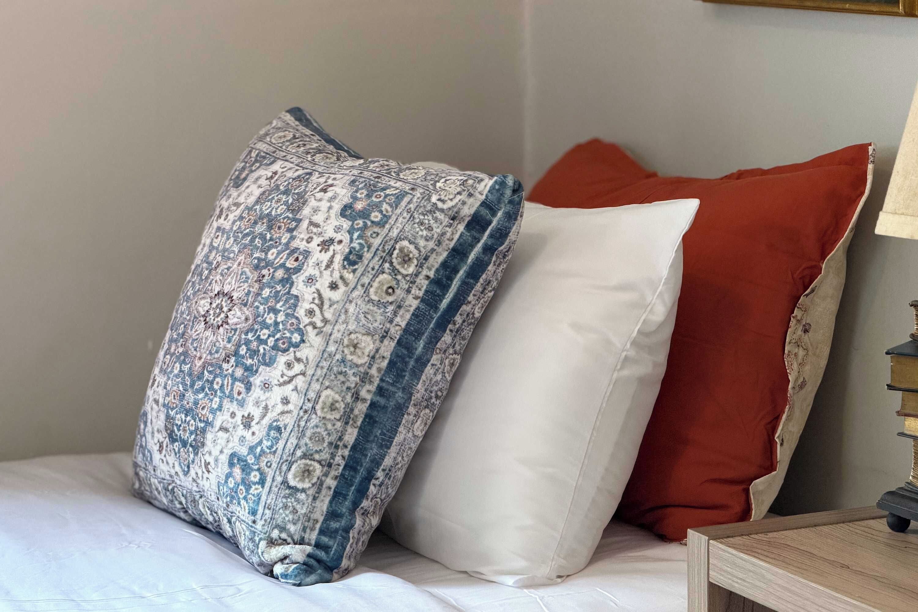 A bed with a patterned pillow and two solid-colored pillows.