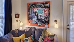 Una sala de estar con un sofá gris, almohadones coloridos, un cuadro abstracto de gran tamaño y dos lámparas de pared.