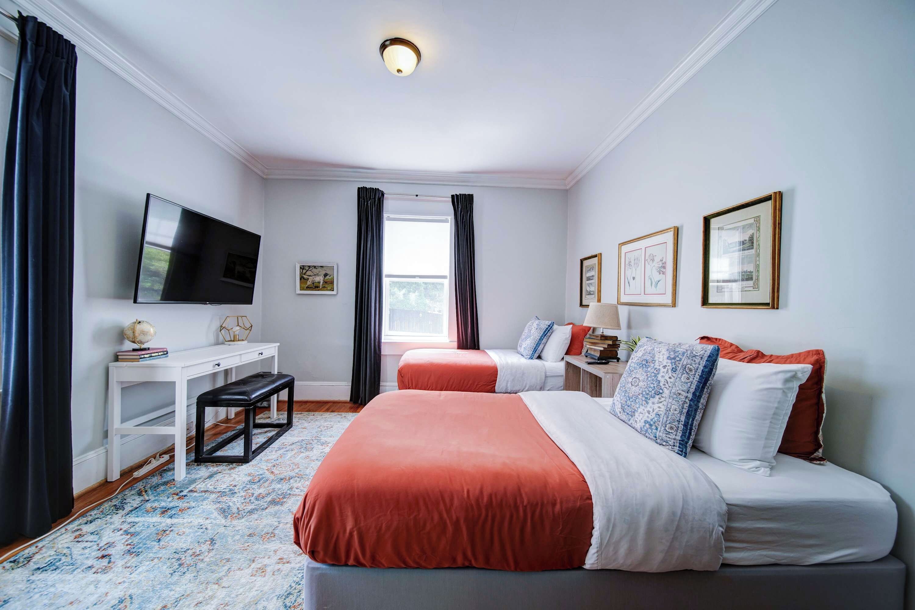 A hotel room with two beds, a TV, a desk, and a window with curtains.