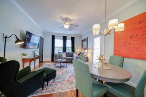 Een moderne woonkamer met een eethoek, voorzien van een plafondventilator, een flatscreen televisie en een groot raam met gordijnen.