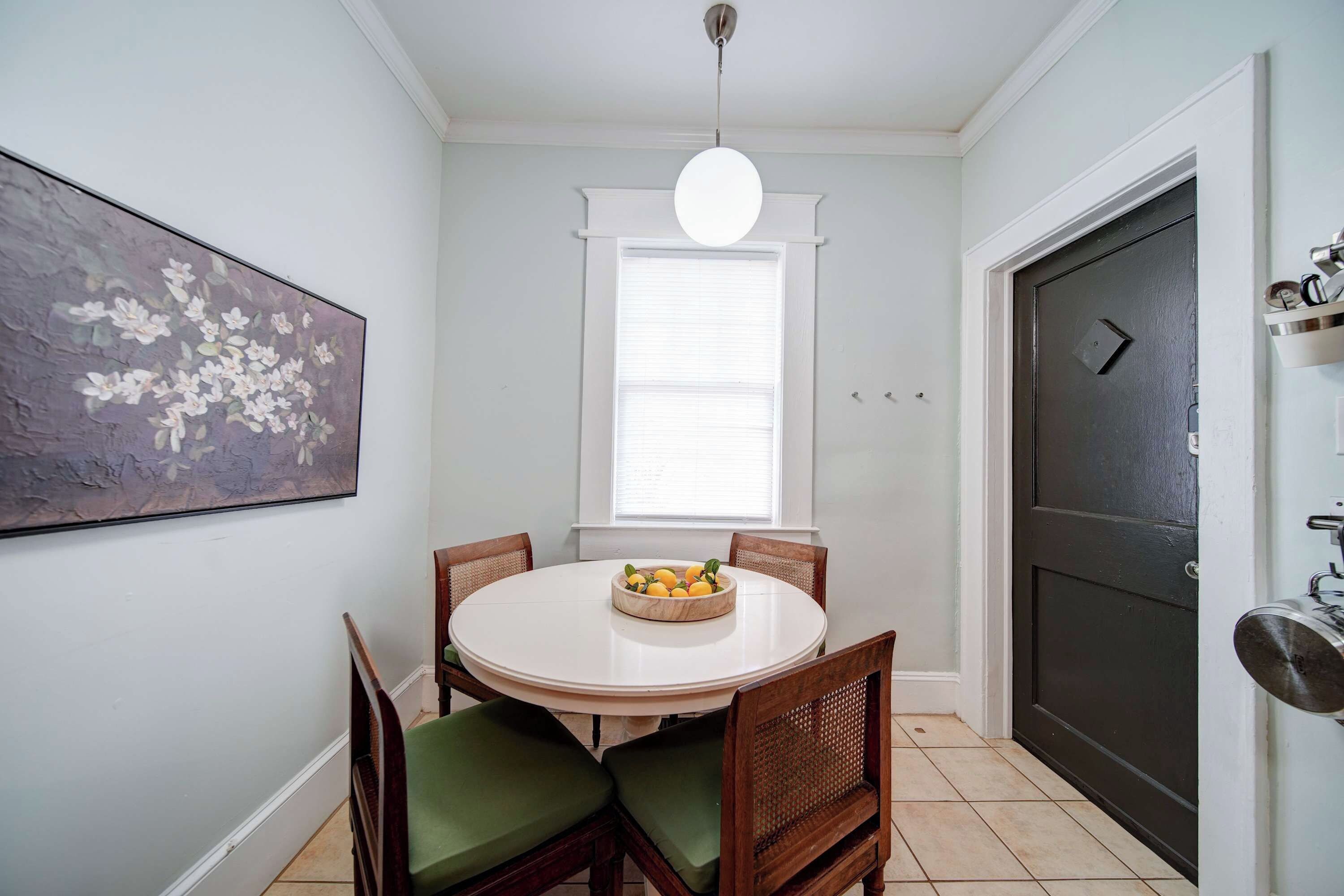 A dining area with a round table, chairs, a fruit bowl, a painting, and a door.