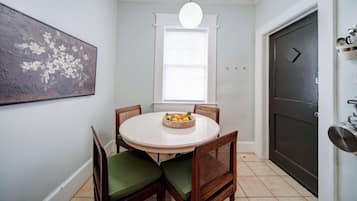A dining area with a round table, chairs, a fruit bowl, a painting, and a door.