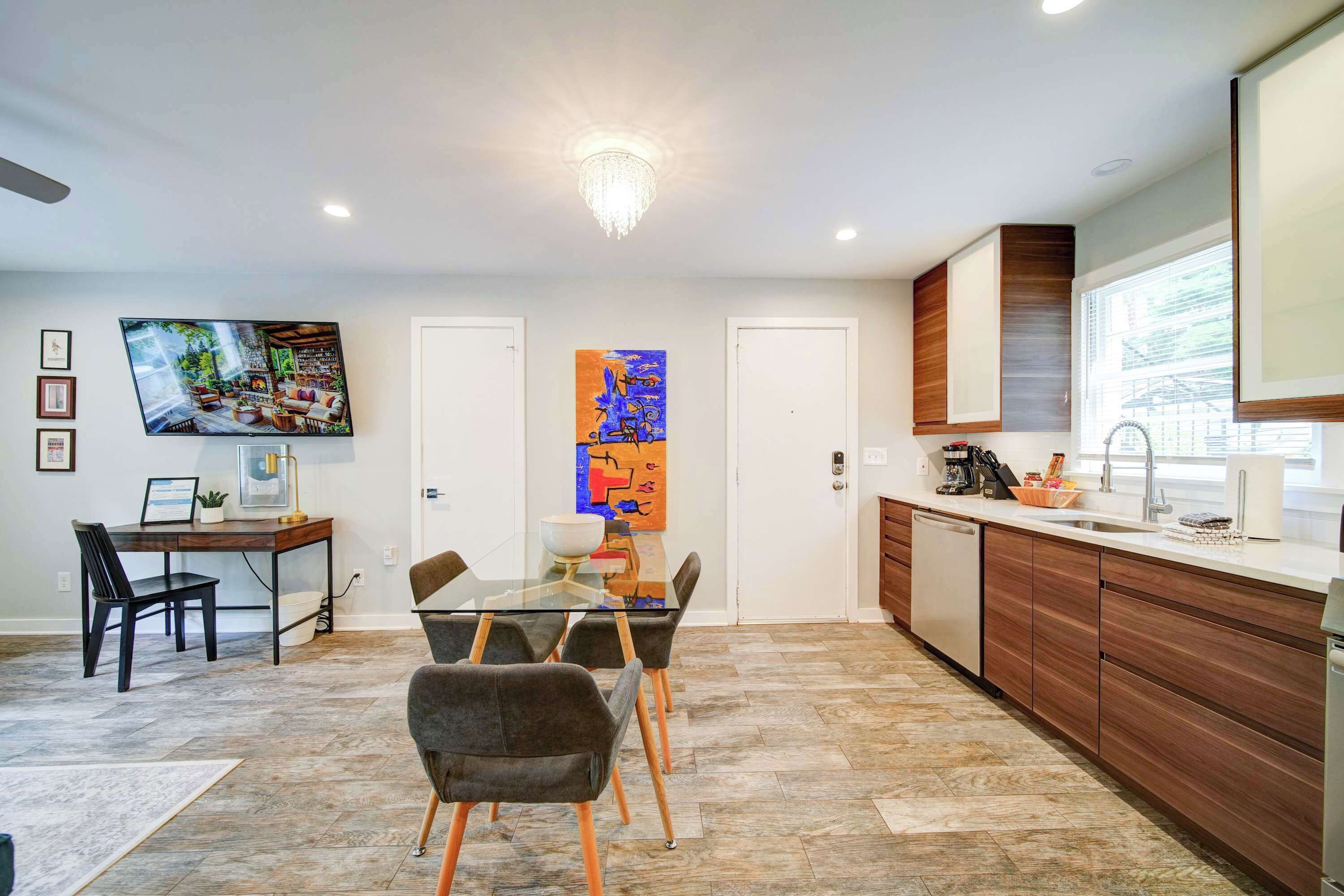 A modern kitchen with a dining area, wooden cabinets, a large window, and artwork on the walls.