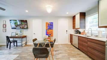 A modern kitchen with a dining area, wooden cabinets, a large window, and artwork on the walls.