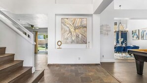 A spacious hallway with a staircase, a pool table, and a dining area with blue chairs. - Extravagant 4BD Home w/ Hot Tub & Pool Table (North Las Vegas)
