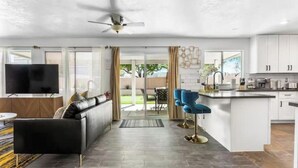 A modern kitchen with white cabinets, a central island, and blue bar stools. - Extravagant 4BD Home w/ Hot Tub & Pool Table (North Las Vegas)