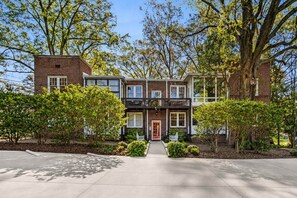 A two-story brick building with a red door, a balcony, and a well-maintained garden.
