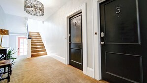 A hallway with a carpeted floor, a staircase, a black door with the number 3, and a decorative light fixture.