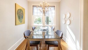 A dining area with a glass table, chairs, a chandelier, and artwork on the walls.