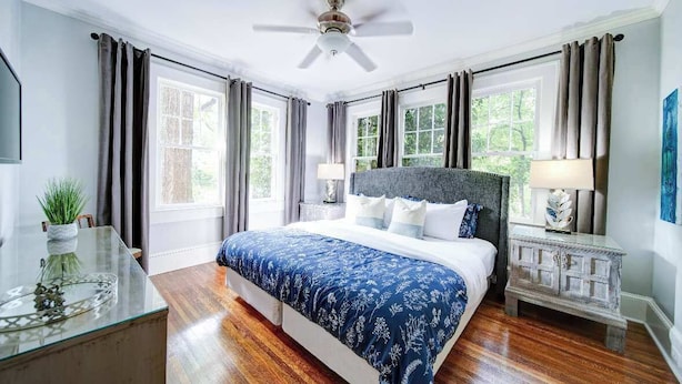 A bedroom with a bed, a ceiling fan, a nightstand, a lamp, and a window.