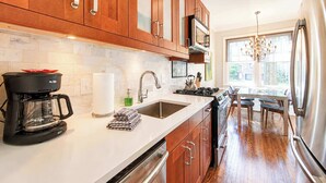 A modern kitchen with wooden cabinets, a stainless steel refrigerator, a coffee maker, and a window providing natural light.
