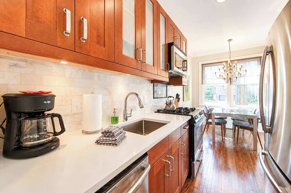 Una cocina moderna con armarios de madera, un refrigerador de acero inoxidable, una cafetera y un ventanal que proporciona luz natural.