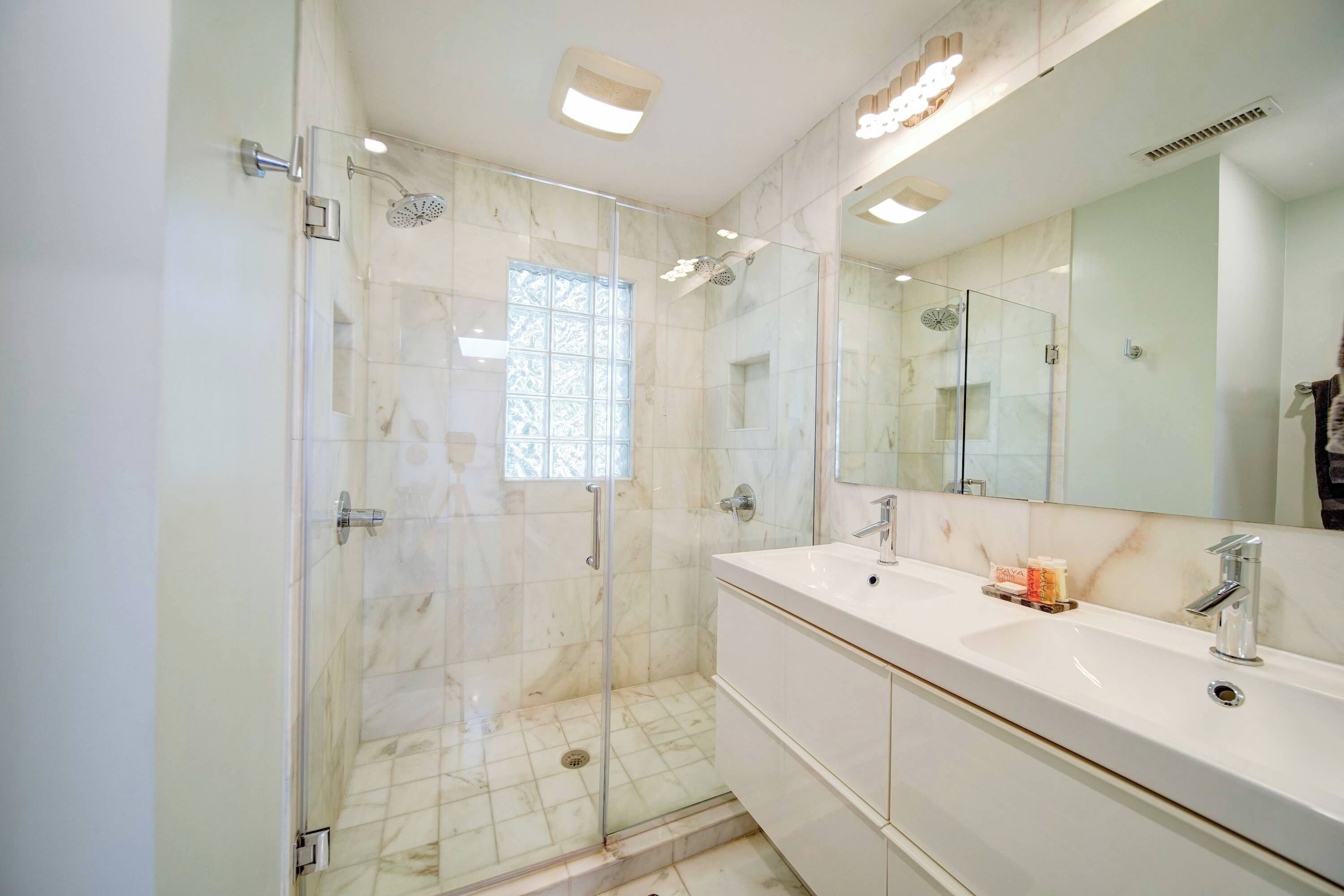 Une salle de bain moderne avec une douche à parois de verre, un grand miroir et un meuble-lavabo blanc.