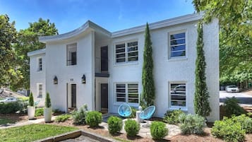 A modern two-story house with a curved facade, numbered 101 and 102, featuring a small front porch with blue chairs and a potted plant.