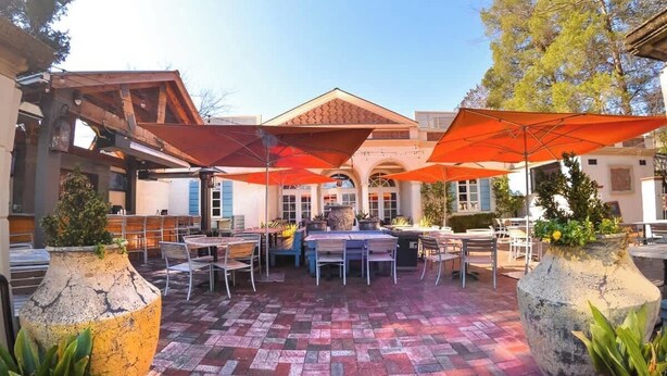 Une terrasse extérieure avec un sol en briques, des tables, des chaises et de grands parasols orange.