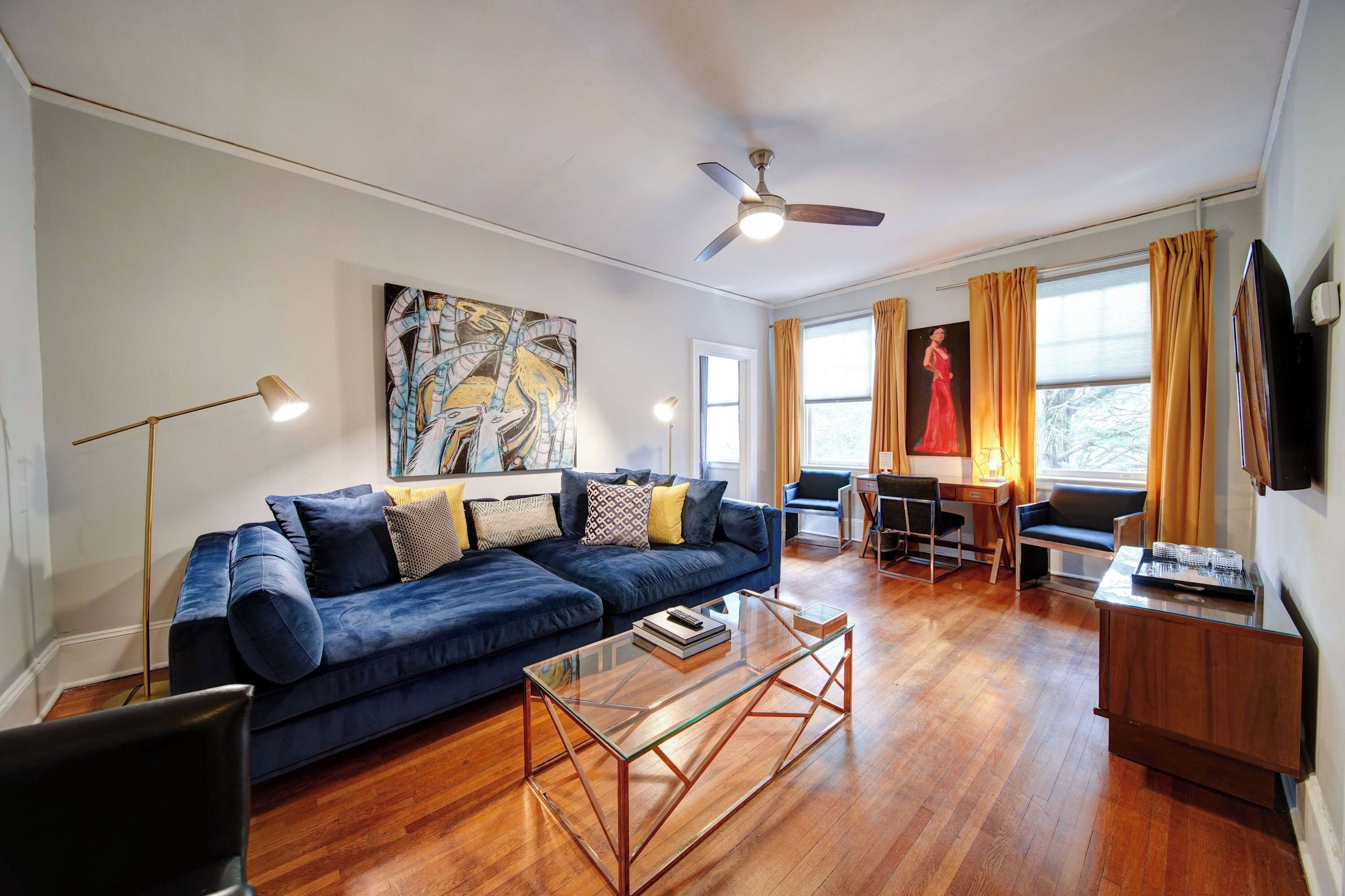 A modern living room with a blue sofa, a glass coffee table, and a ceiling fan.