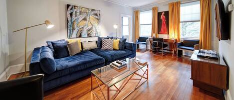 A modern living room with a blue sofa, a glass coffee table, and a ceiling fan.