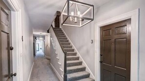 Un pasillo con una escalera, una puerta con el número 3 y un candelabro sobre la escalera.