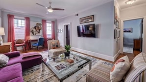 Una sala de estar con sofá, sillón, mesa de centro y televisor montado en la pared.