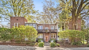 A two-story brick house with a front porch, a small front yard, and a driveway. - Charming Condo Near Freedom Park | King Bed & Screened Porch (Charlotte)