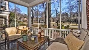 A covered porch with a wooden table, two sofas, and a potted plant. - Charming Condo Near Freedom Park | King Bed & Screened Porch (Charlotte)