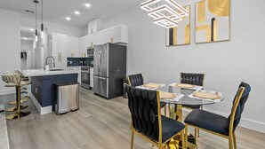 A modern kitchen with white cabinets, stainless steel appliances, and a central island. There is a dining area with a table and chairs, and artwork on the wall. - Spacious ,Luxury 3-bedroom apartment in Houston with Games ,Smart Tv,Wifi (Houston)